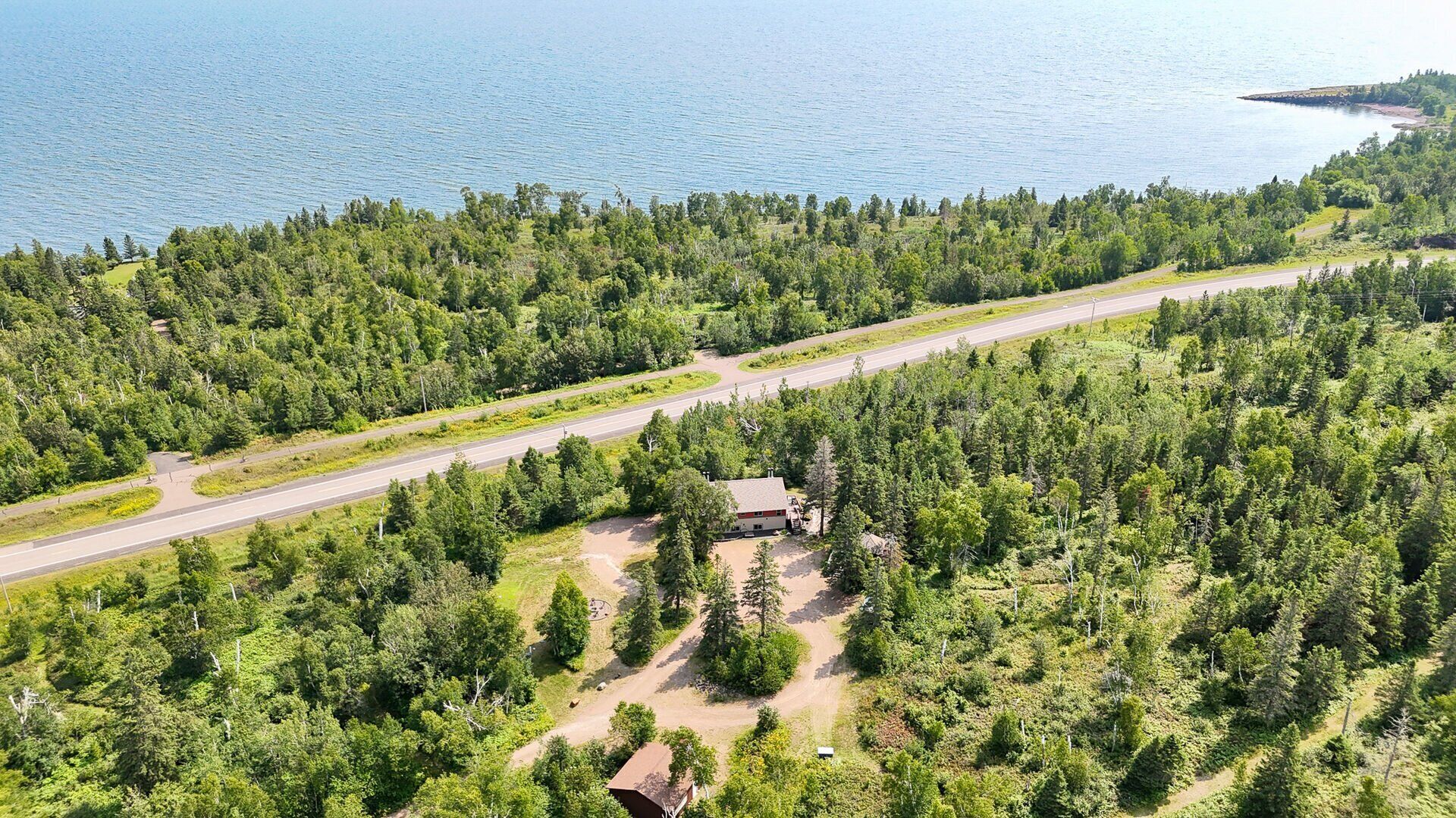 An aerial view of a forested area with a road, a small building, and a body of water.