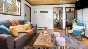 Ein gemütliches Wohnzimmer mit Holzbalkendecke, einer Couch mit bunten Kissen, einem Couchtisch und einem gemusterten Teppich.