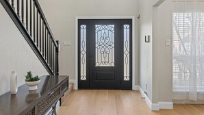 Une porte noire ornée de panneaux de verre décoratifs, un escalier en bois sur la gauche et un mur blanc.