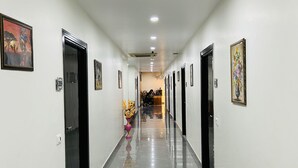 A long, narrow hallway with white walls and black doors, lined with framed artwork and a central floral arrangement. - Hotel Green Plaza (Sonepat)