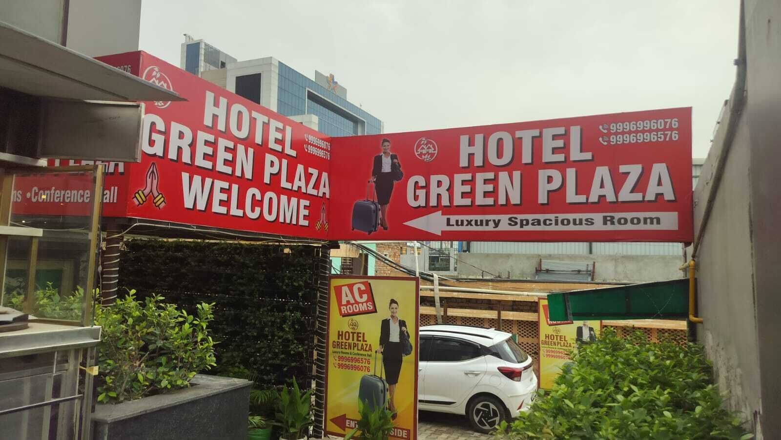 A hotel sign for Hotel Green Plaza with a welcome message and contact numbers.