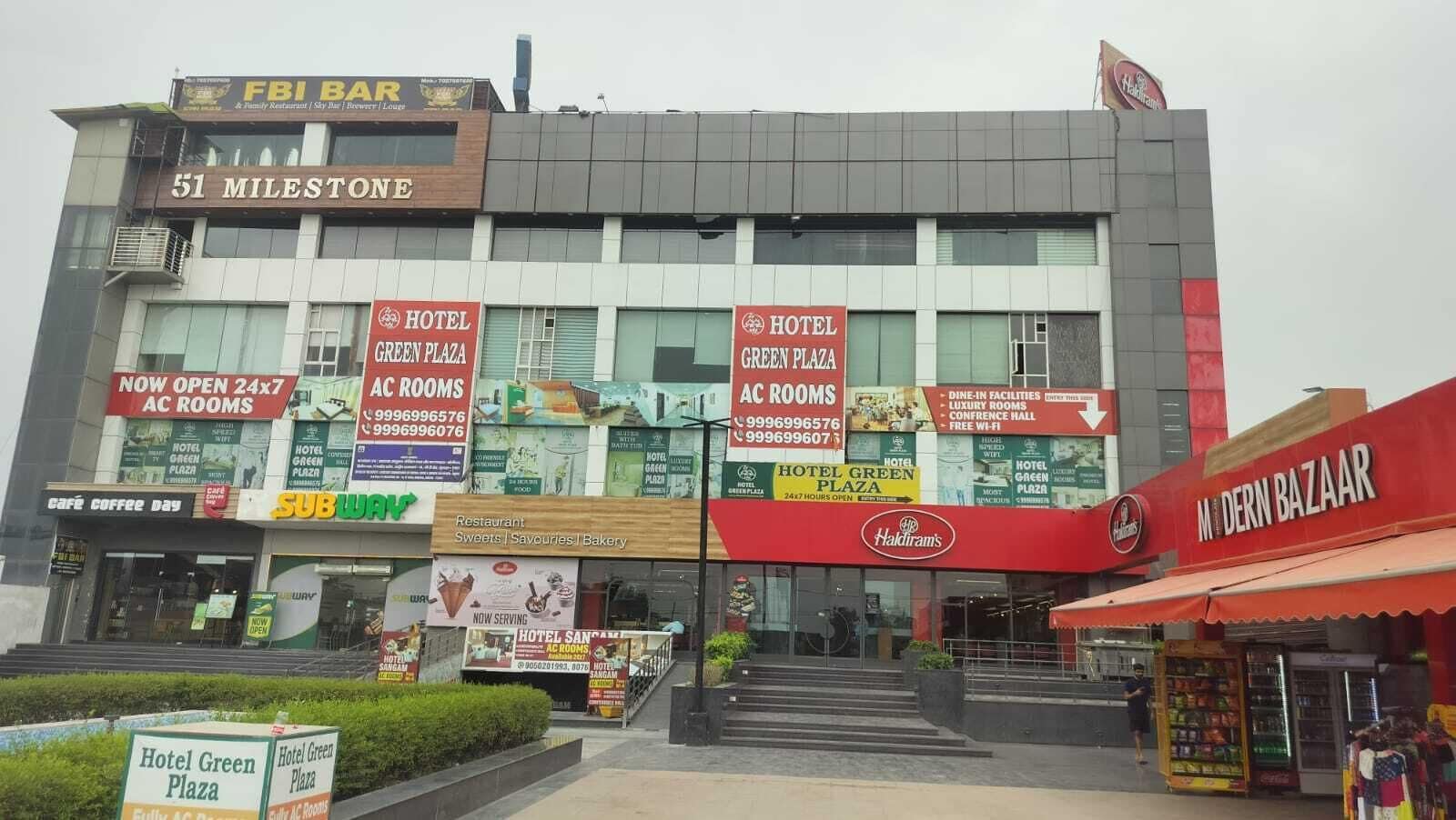 A hotel named 'Hotel Green Plaza' with multiple signs advertising 'AC Rooms' and '24x7 AC Rooms'.