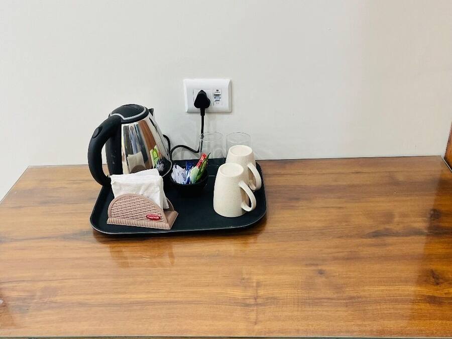 Una mesa de madera con una bandeja negra que contiene una tetera, un paquete de pañuelos de papel y dos tazas blancas.