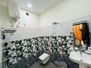 Un baño con ducha, inodoro y lavamanos, que cuenta con un salpicadero de azulejos estampados y suelo de mármol.