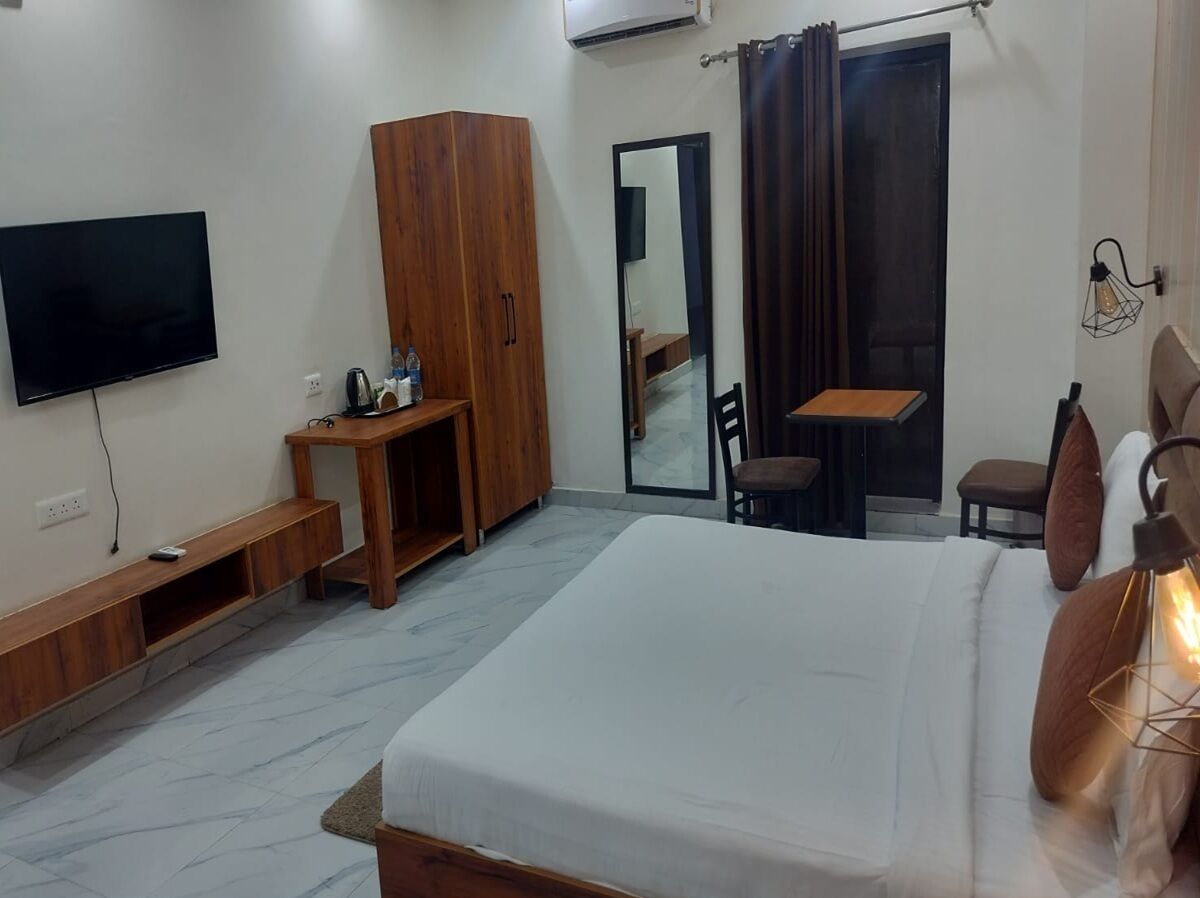 Quarto de hotel com cama, televisão, guarda-roupa de madeira, secretária, cadeira e espelho.