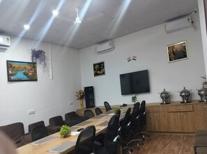 Un salón de conferencias con una mesa larga, sillas, un televisor de pantalla plana, elementos decorativos y unidades de aire acondicionado fijadas a la pared.