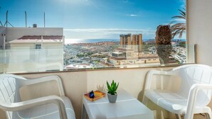 Un balcón con dos sillas de plástico blanco, una mesa pequeña y una planta en maceta.