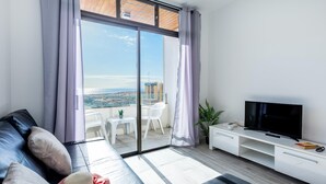 Una sala de estar moderna con sofá, televisión y balcón con vista a la ciudad.