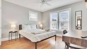 Une chambre à coucher comprenant un lit, des tables de chevet, un bureau et un ventilateur de plafond.