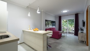 A modern kitchen with a central island, a dining area with a red sofa, and a balcony with a view of greenery. - Apartment in Mogan Near Playa de Mogan (Mogan)