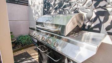 A stainless steel outdoor grill with a digital display, located in a patio area with a decorative wall and a small garden.