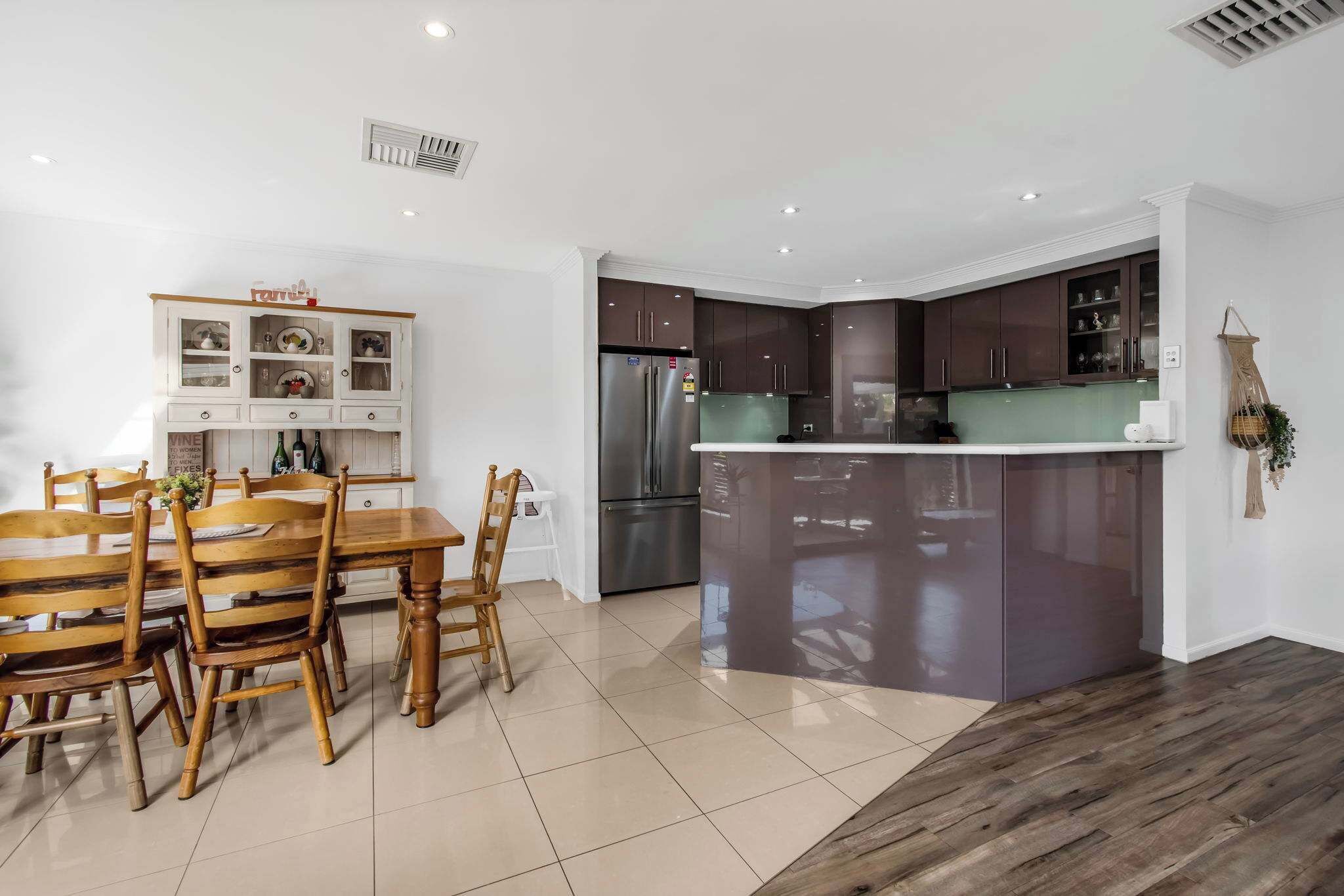 A modern kitchen with dark cabinets, a stainless steel refrigerator, and a wooden dining table with chairs.