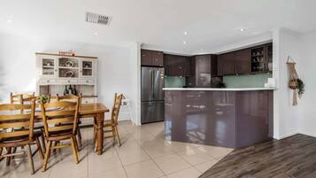 A modern kitchen with dark cabinets, a stainless steel refrigerator, and a wooden dining table with chairs.