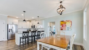 A spacious kitchen with white cabinets, a stainless steel refrigerator, and a wooden dining table with white chairs.