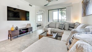 A modern living room with a large flat-screen TV, a sofa, a coffee table, and a TV stand with decorative items. - Golfer’s Paradise! Extended-Stay Bradenton Condo (Bradenton)