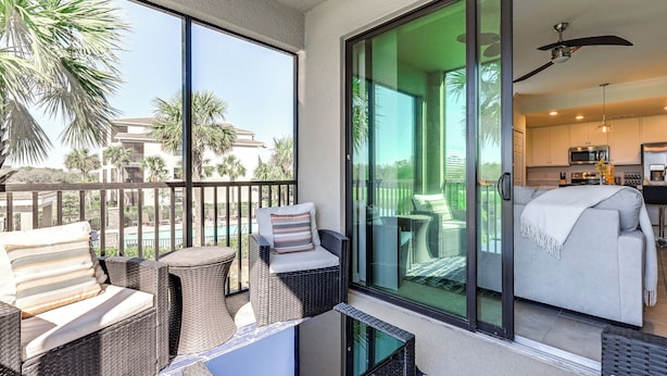 A balcony with wicker furniture, a glass door leading to a living area with a sofa and a ceiling fan. - Golfer’s Paradise! Extended-Stay Bradenton Condo (Bradenton)