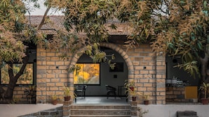 A stone building with a tiled roof, a covered patio area with chairs, and potted plants. - Aatman Forest Resort – A Luxury Stay in Sasan Gir (Talala)