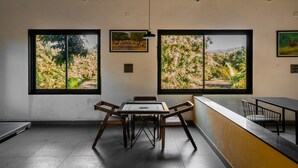 A room with a table and chairs, large windows with natural light, and a view of trees and hills. - Aatman Forest Resort – A Luxury Stay in Sasan Gir (Talala)