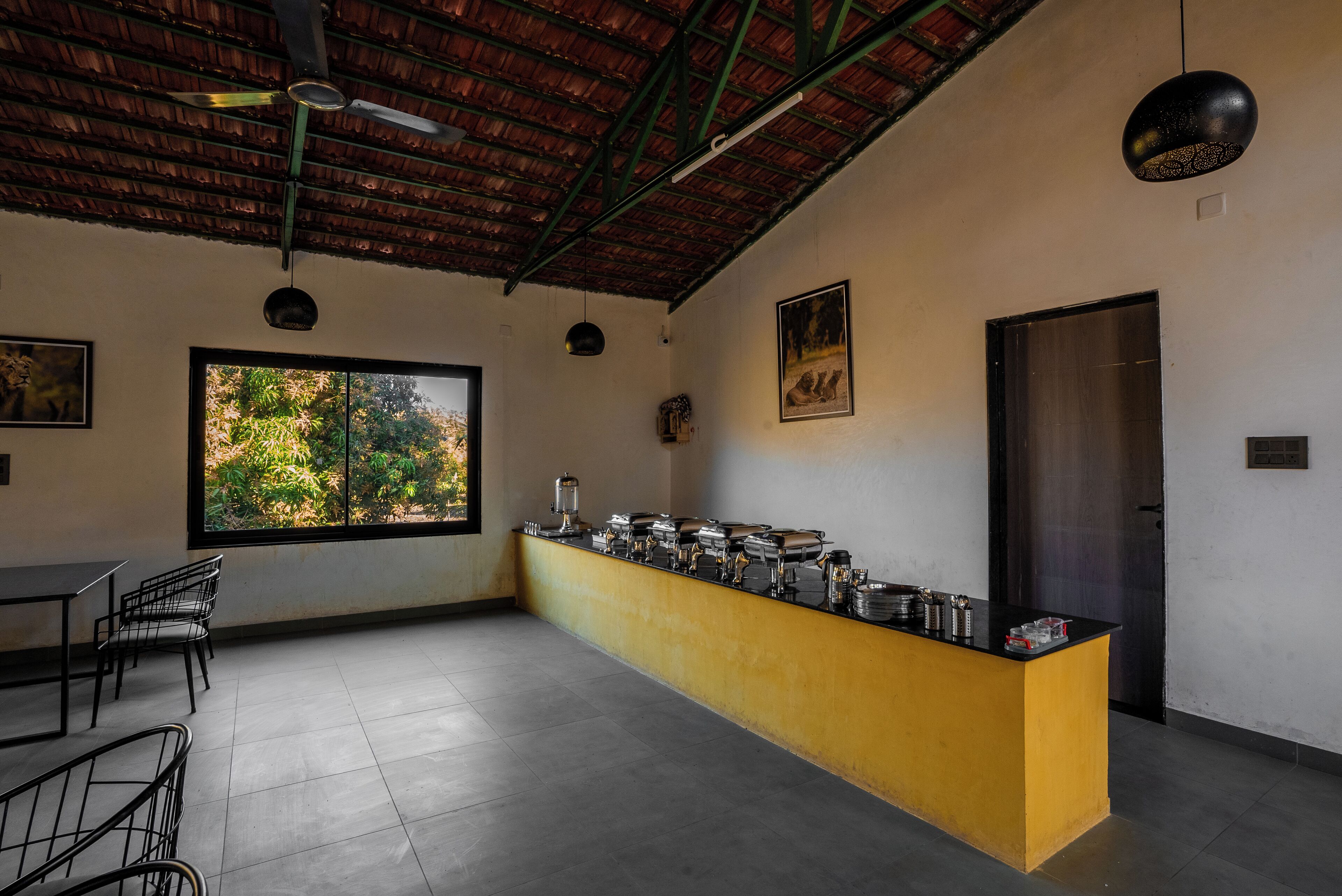 A room with a long counter, chairs, a ceiling fan, and a large window with a view of trees.