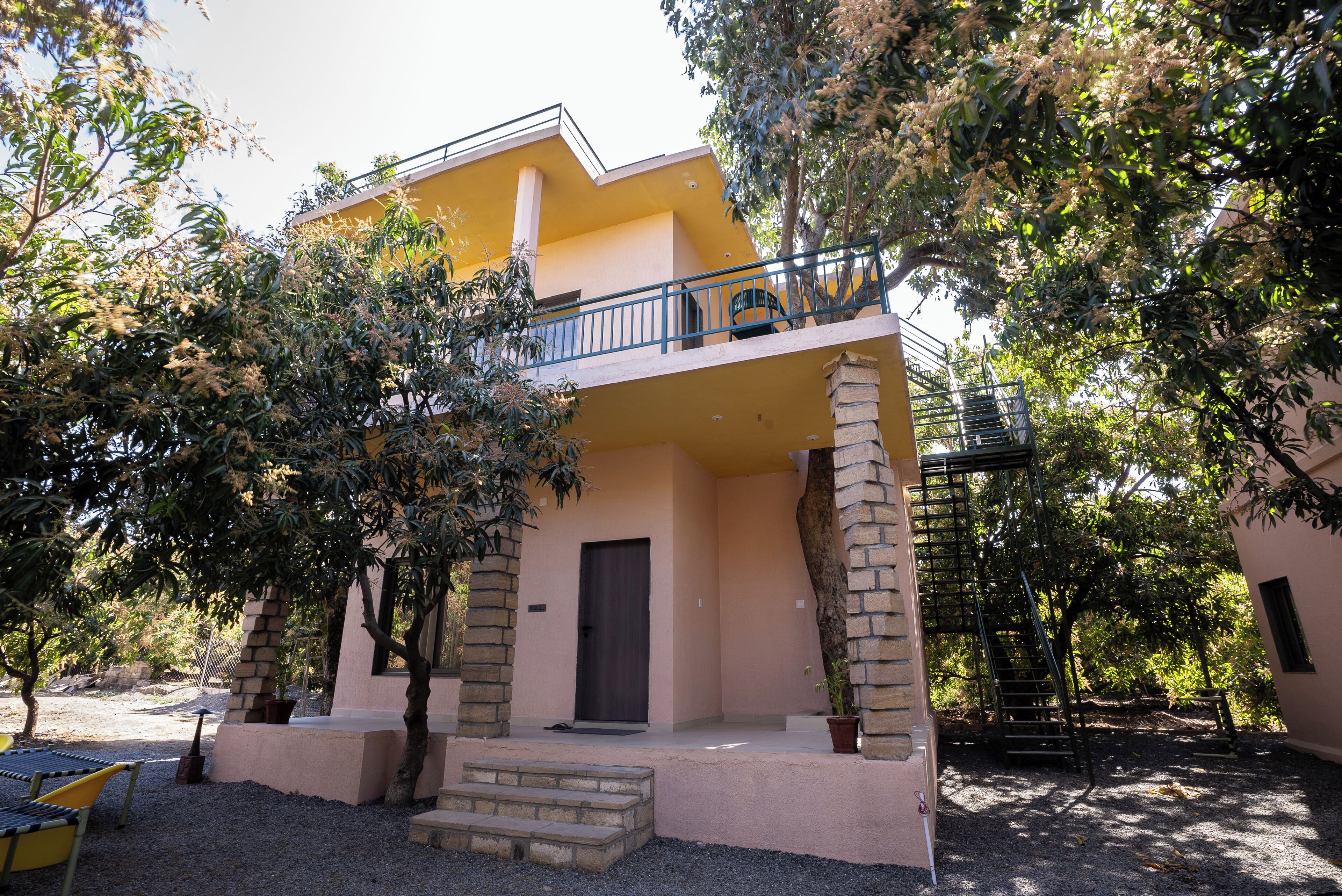 A two-story building with a balcony, surrounded by trees and a gravel driveway.
