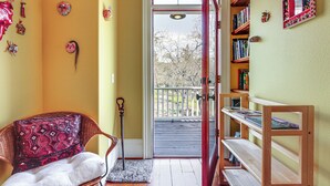 Een kamer met een rieten stoel, een boekenkast en een deur naar een balkon.
