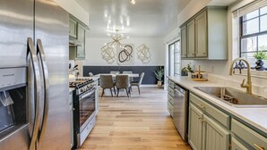 Una cocina moderna con electrodomésticos de acero inoxidable, una zona de comedor con mesa y sillas, y un ventanal que proporciona luz natural.