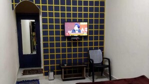 Une chambre d’hôtel avec un lit, un téléviseur fixé au mur, une chaise, une petite table et un tapis décoratif.
