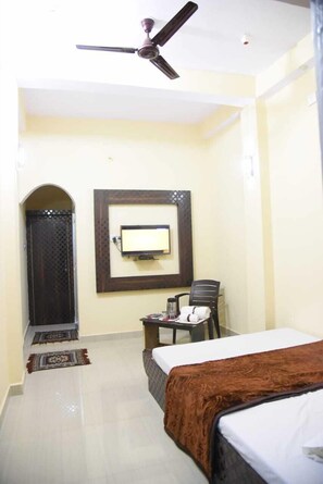Une chambre d’hôtel équipée d’un lit, d’un bureau, d’une chaise, d’un téléviseur fixé au mur et d’un ventilateur de plafond.