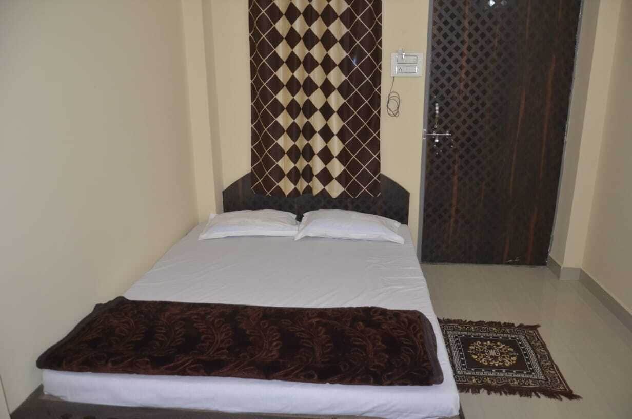 A single bed with white linens, a dark brown throw blanket, and a patterned rug on a tiled floor.