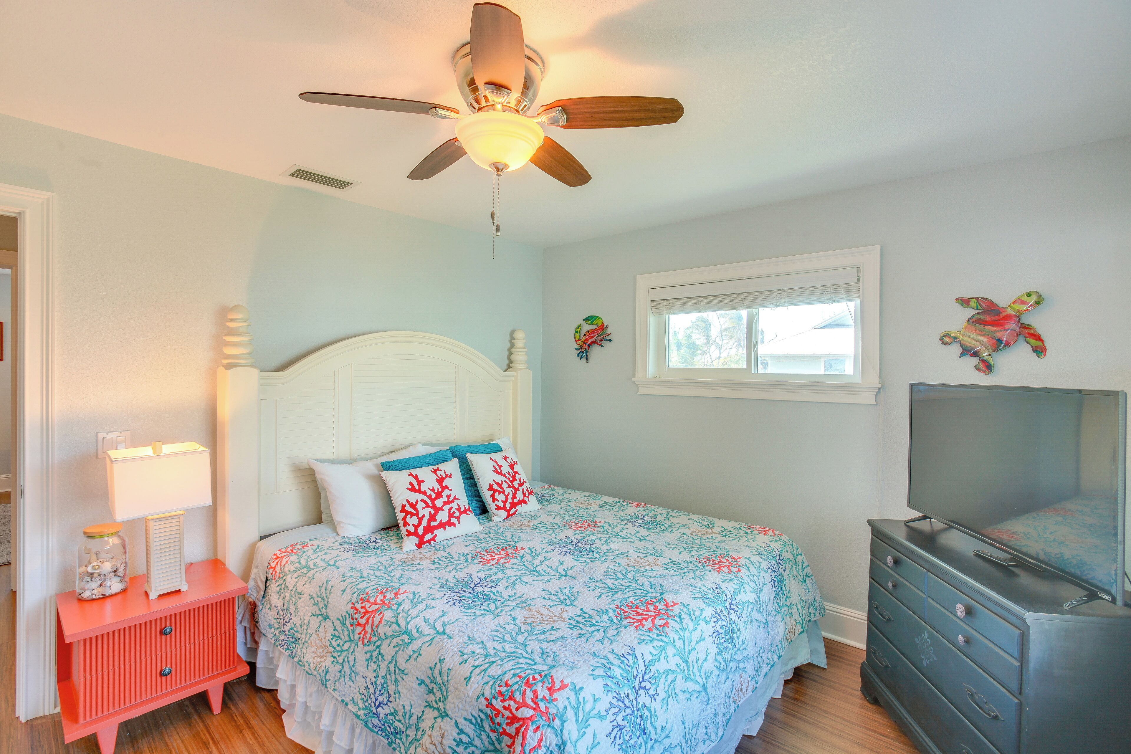 Un dormitorio con cama, cómoda, ventilador de techo, ventana y decoración mural.