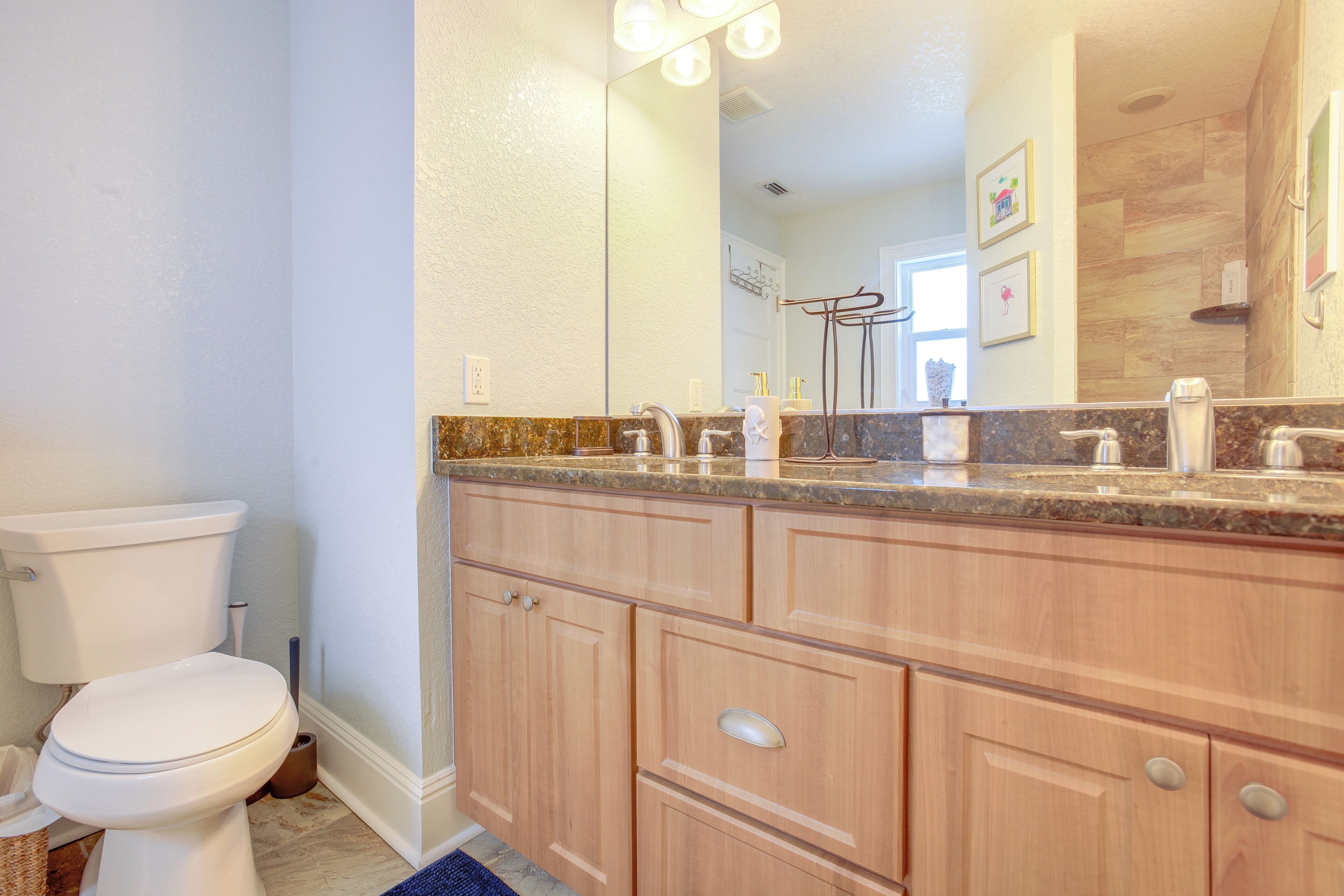 A bathroom with a toilet, wooden cabinets, a marble countertop, and a mirror.
