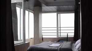 Un dormitorio moderno con una cama grande, ventilador de techo y ventanas amplias.