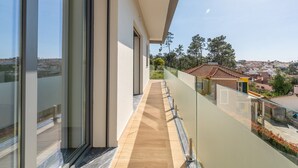 A modern balcony with large windows, a wooden floor, and a view of a town.