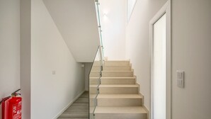 A staircase with glass railings leading to a landing, a fire extinguisher on the left, and a door on the right.