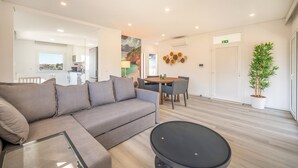 A modern living room with a grey sectional sofa, a round coffee table, and a dining area with a table and chairs.