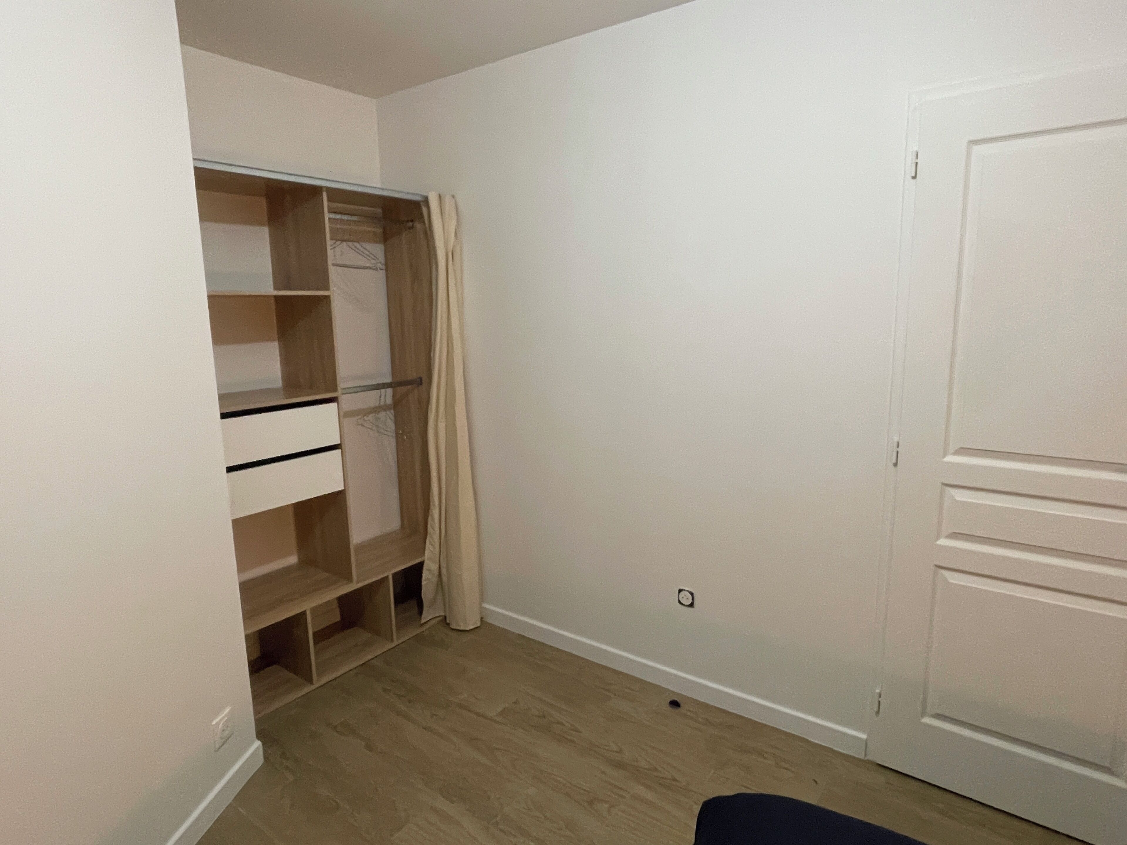 Une pièce avec un plancher en bois, une porte blanche et un placard doté d’étagères et d’une tringle pour suspendre les vêtements.