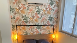 Ein Schlafzimmer mit einem Bett, zwei Nachttischlampen, einer Wand-Klimaanlage und einem Fenster.