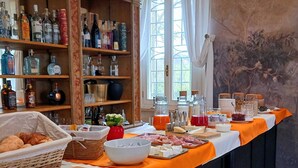 A buffet setup with various food items and beverages, a wicker basket of bread, and a wine and liquor shelf in the background. - Tuscany Garden Inn (Castel San Pietro Terme)