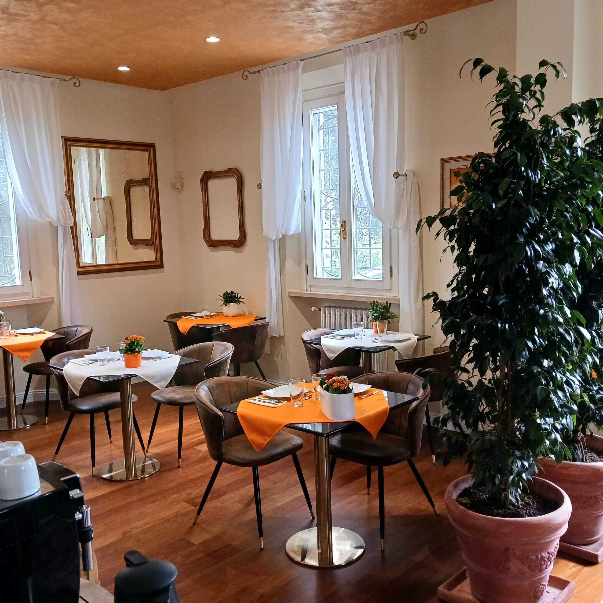 A dining area with tables set for two, wooden flooring, and potted plants.