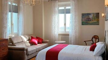 A bedroom with a bed, a sofa, a chair, a dresser, a chandelier, and a painting.