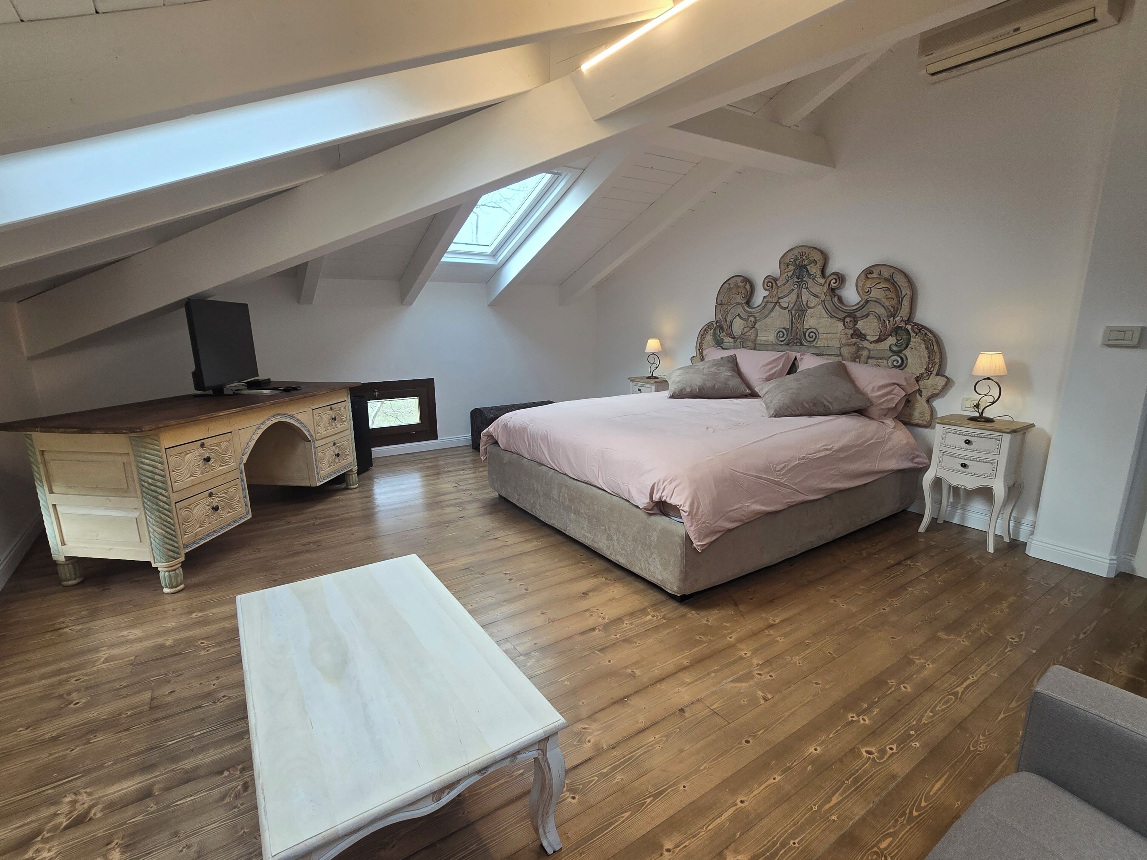 Una camera da letto con soffitto a falde, un letto con testiera, una cassettiera, una TV e un tavolino.