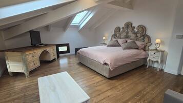Una camera da letto con soffitto a falde, un letto con testiera, una cassettiera, una TV e un tavolino.