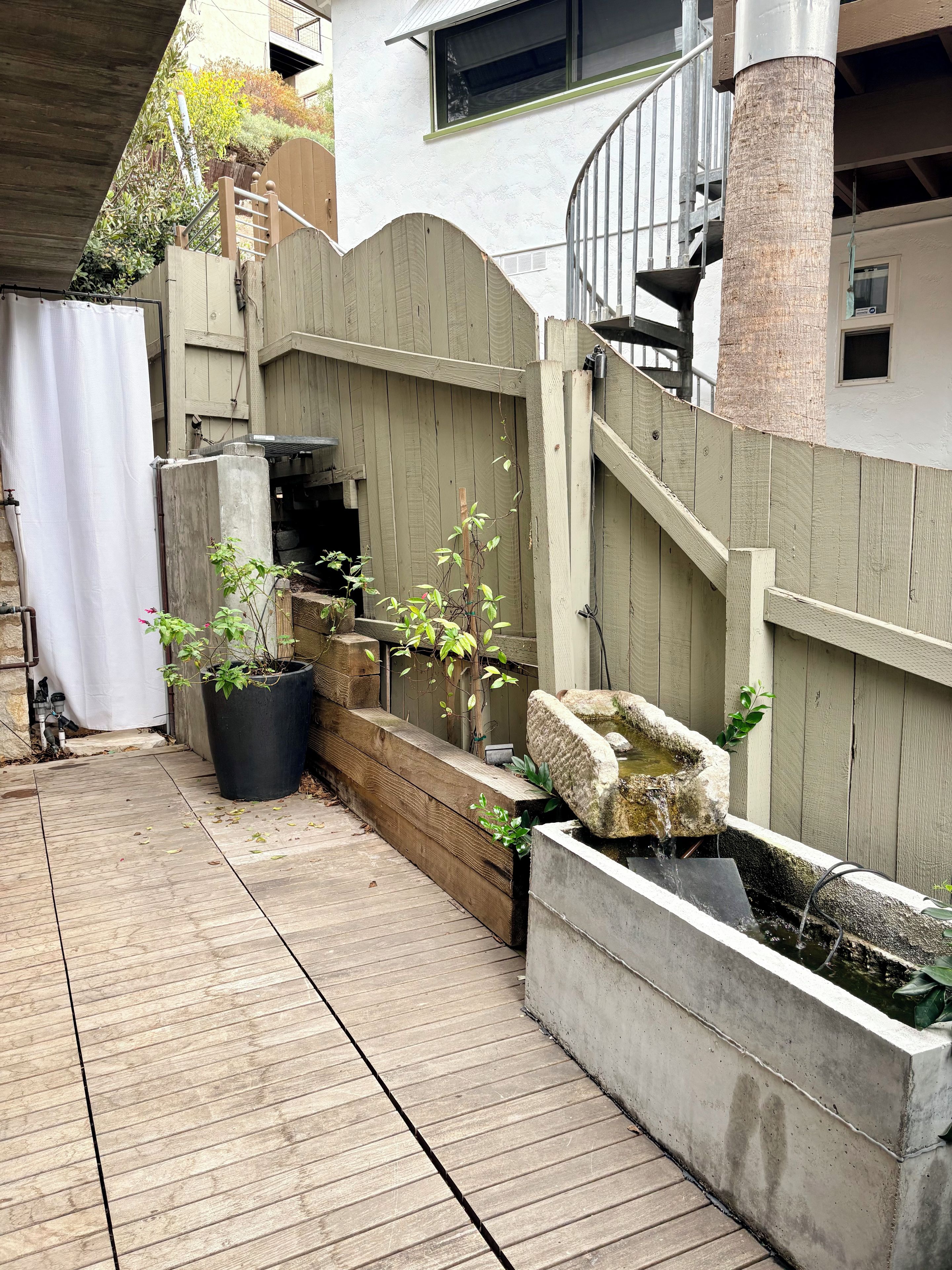 Une terrasse en bois agrémentée d’un bac à fleurs en béton et d’un petit élément décoratif aquatique.