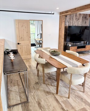 A modern living room with a wooden dining table, comfortable seating, a flat-screen TV, and a view of the outdoors. - Cali beach living! Modern 2 BR home. Pet friendly. Walk to town, beaches, harbor (Dana Point)