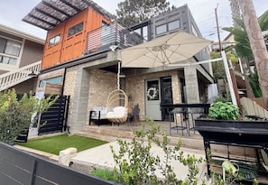 Une maison moderne à deux étages, dotée d’une façade en pierre, d’un balcon et d’un patio aménagé avec du mobilier d’extérieur.