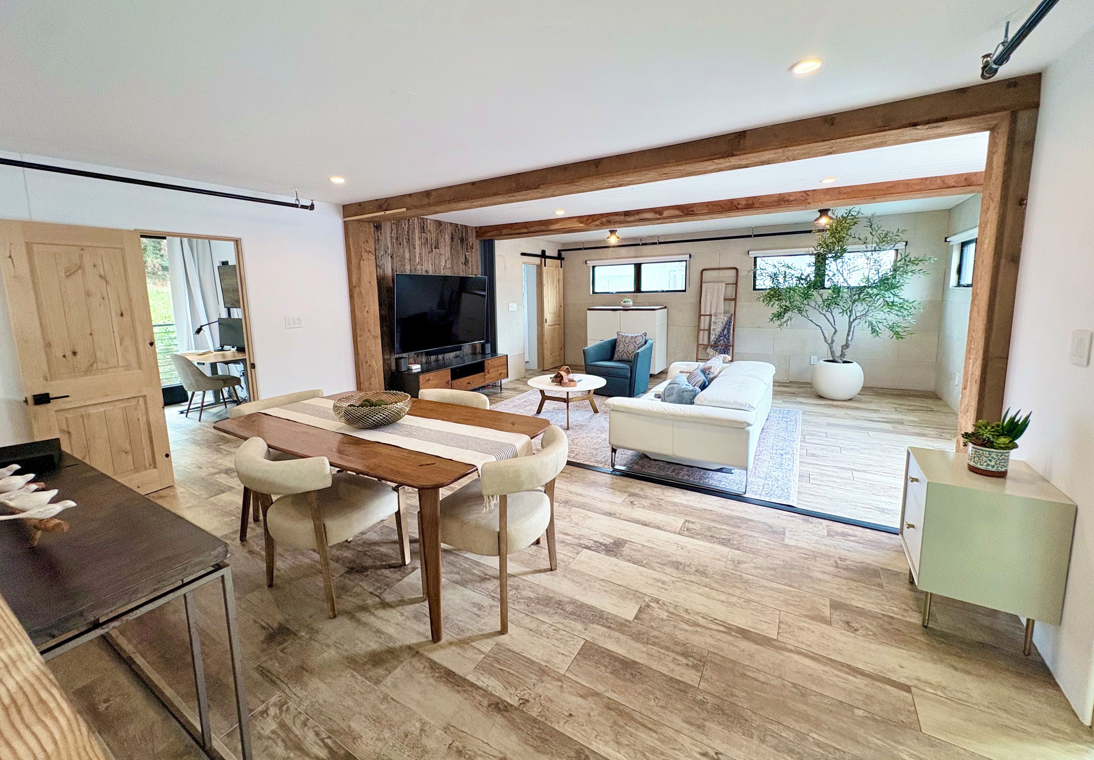 A spacious living area with a wooden dining table, a sofa, and a television.