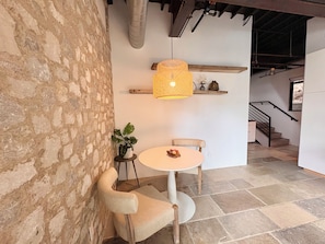 Une pièce avec un mur en pierre, une table ronde avec une chaise, un luminaire suspendu et un escalier en arrière-plan.