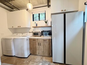 A compact kitchen with a washing machine, a microwave, and a double-door refrigerator. - Cali beach living! Modern 2 BR home. Pet friendly. Walk to town, beaches, harbor (Dana Point)