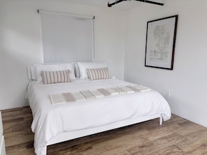 Un lit avec une tête de lit blanche, deux oreillers, un couvre-lit blanc et un plaid décoratif.