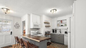 A modern kitchen with white cabinets, a wooden island with bar stools, a gas stove, and a microwave. - [New Listing] Walk To Beach, Main St, Harbor. Beautifully Renovated - Captain Gosnold Village (Hyannis)